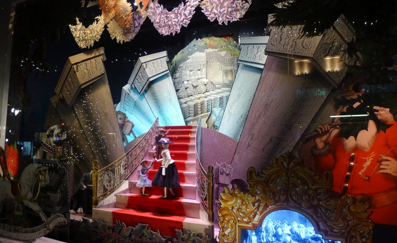 A royal Christmas window display with a castle layout, and two dolls climbing the stairs.