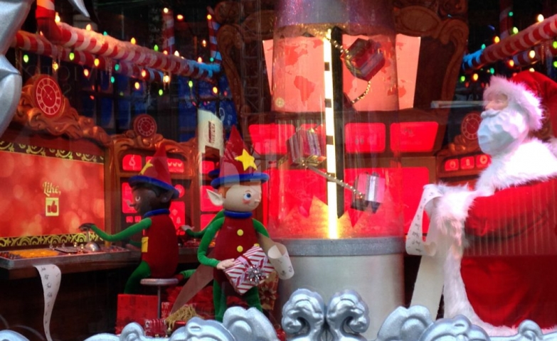On a red decor, in this window display, Santa is talking with his best elf about the Christmas list of gifts.