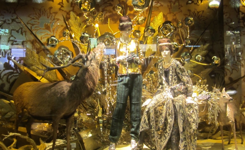 In this Christmas window display, we can see two mannequins near a deer, and many golden details, in theme with the holidays.