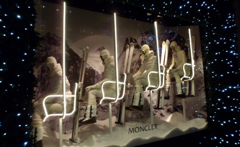 Skiers dressed in a white ski suit, looking futuristic on the chairlift, surrounded by Christmas lights for the window display.