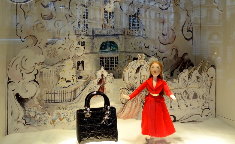 A  window display with a puppet dressed in red, ready for Christmas night, and an elegant bag, near the puppet.