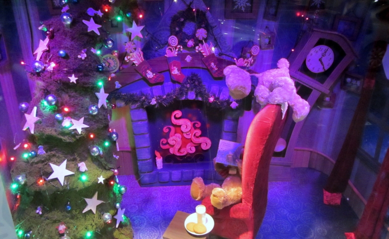 A window display, which describes a typical Christmas night, with some teddy bears waiting for Santa with milk and cookies near the adorned tree.